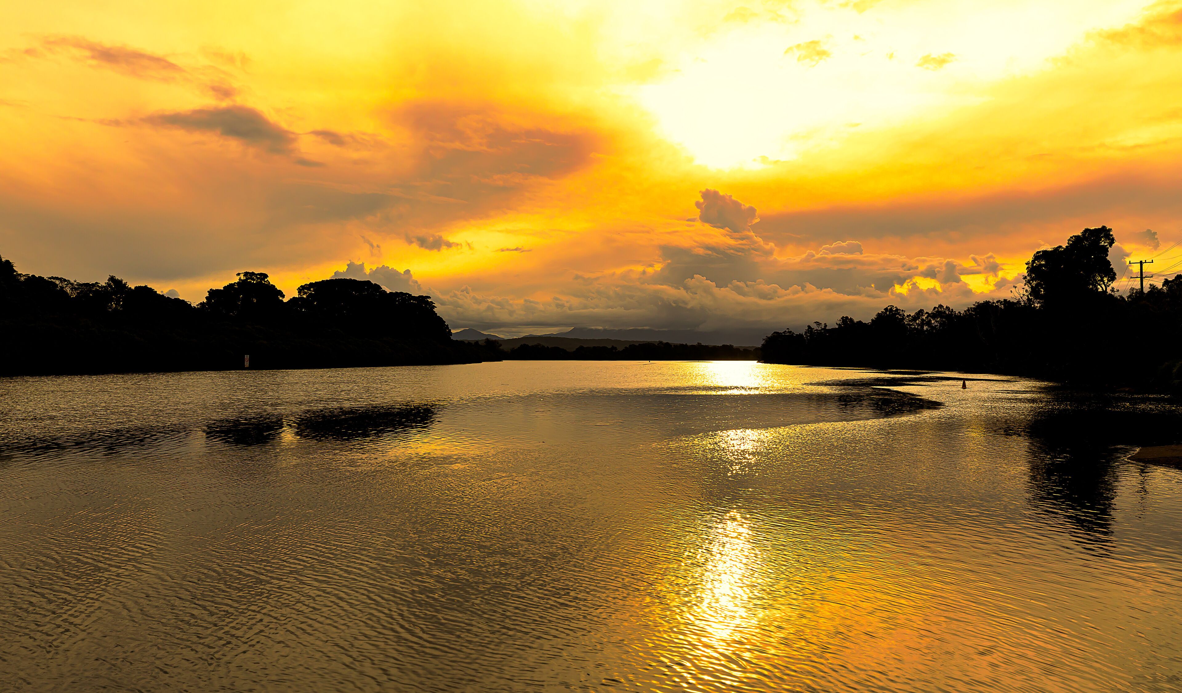 Brilliant golden sunlight of a late afternoon highlights the cloud formations and creates beautiful reflections in the calm waters of a coastal river, Mylestom ,NSW ,Australia.