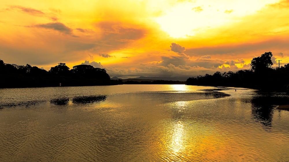 Brilliant golden sunlight of a late afternoon highlights the cloud formations and creates beautiful reflections in the calm waters of a coastal river, Mylestom ,NSW ,Australia.