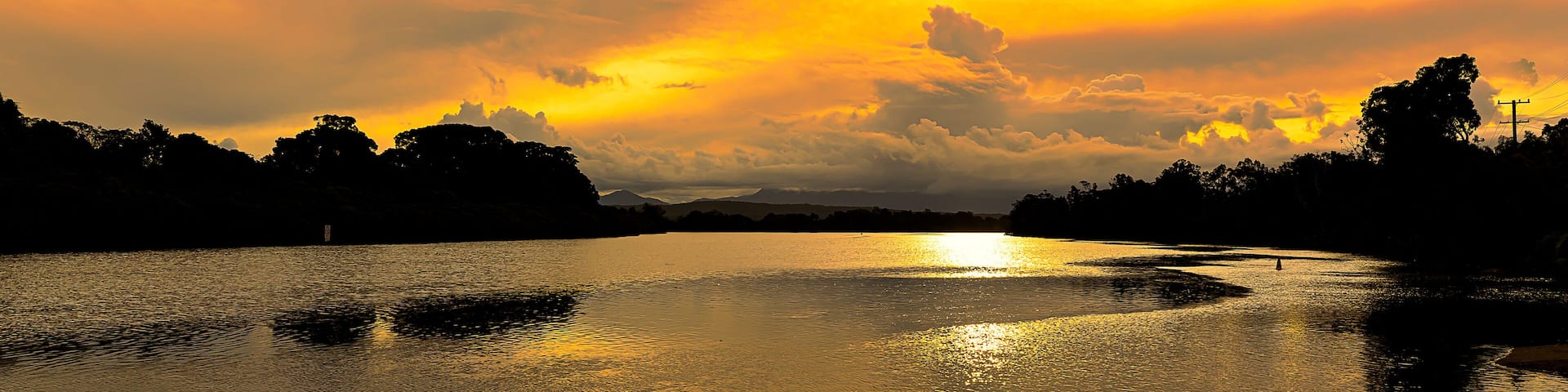 Brilliant golden sunlight of a late afternoon highlights the cloud formations and creates beautiful reflections in the calm waters of a coastal river, Mylestom ,NSW ,Australia.