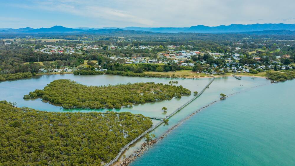 An aerial view of a coastal area with a large body of water, a bridge, and a dense forest.