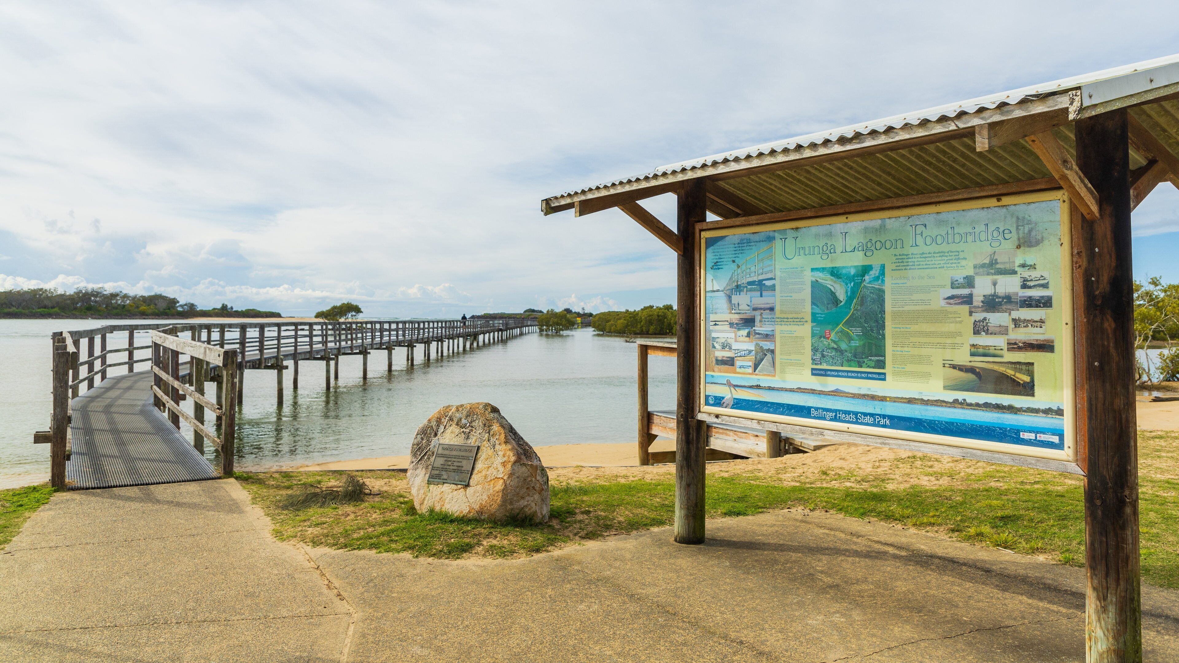 A wooden pier extending into a calm lake, a signboard with historical information, and a rocky outcrop in the foreground.