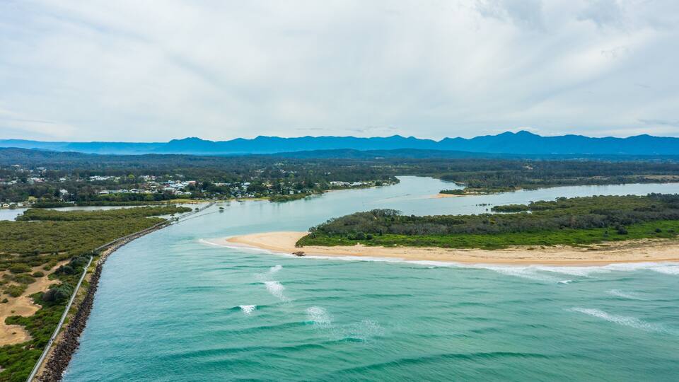 A coastal landscape with a river, beach, and mountains in the background.
