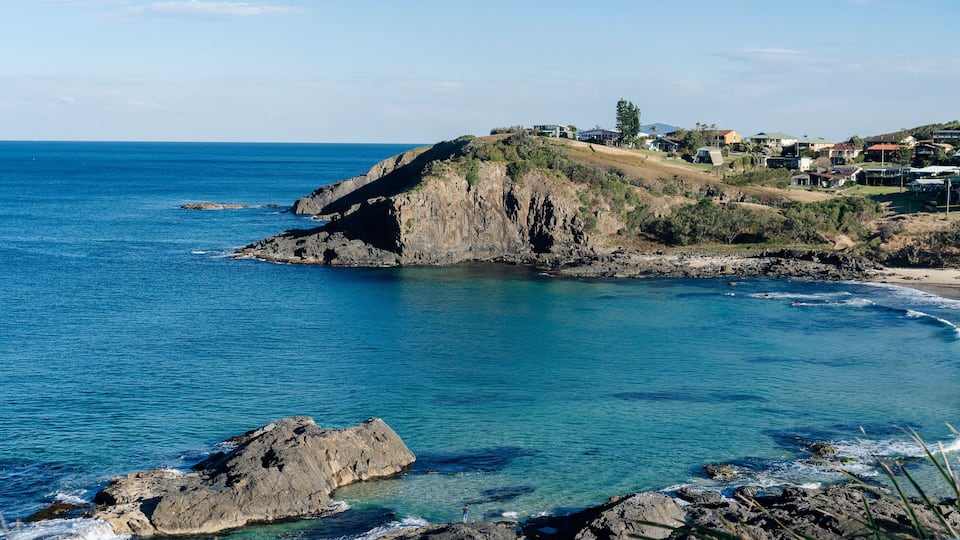A coastal landscape with rocky cliffs, clear blue waters, and a small settlement on the hillside.