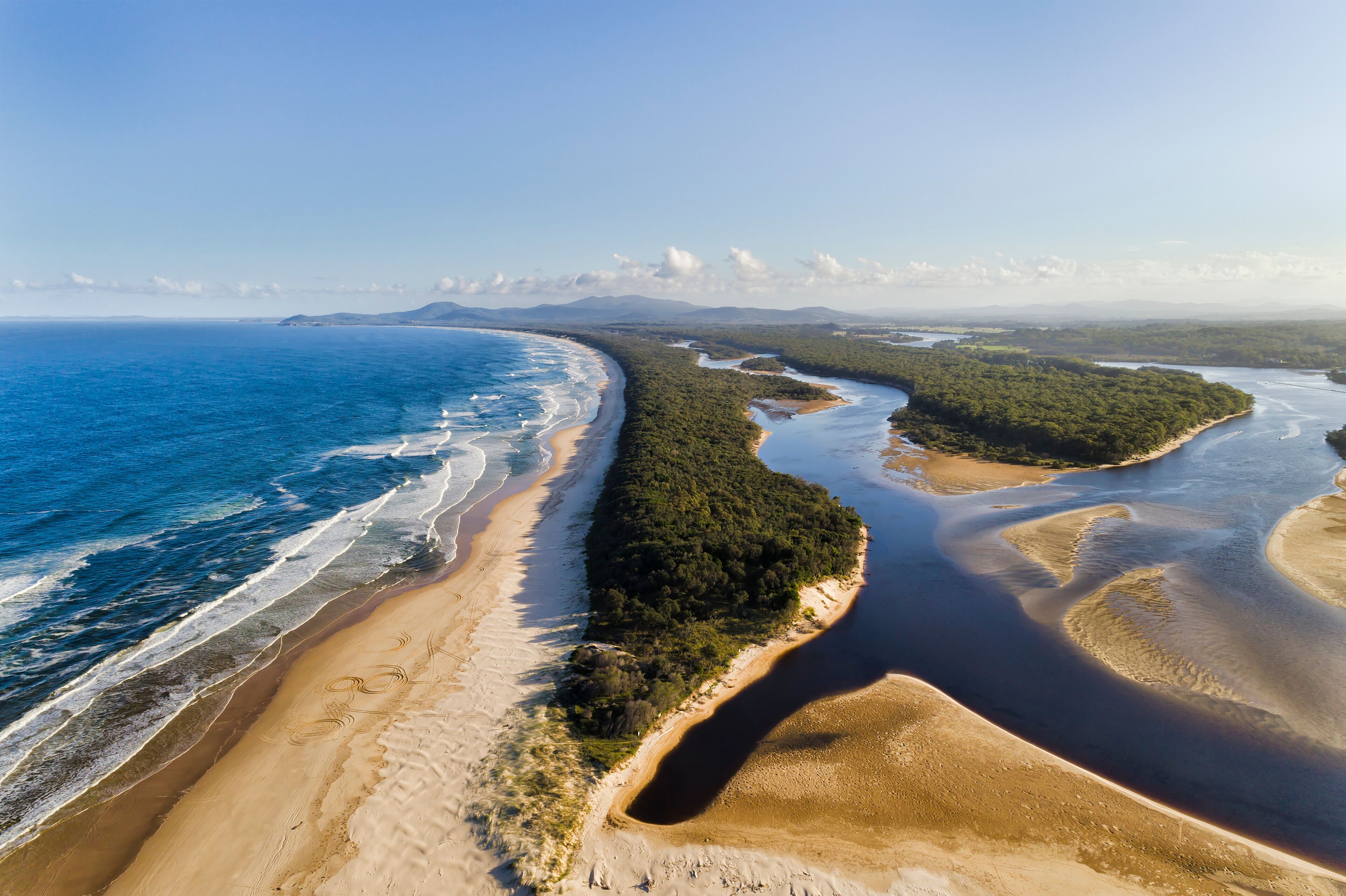 Un paysage côtier comprenant une plage de sable, une rivière et une zone boisée.