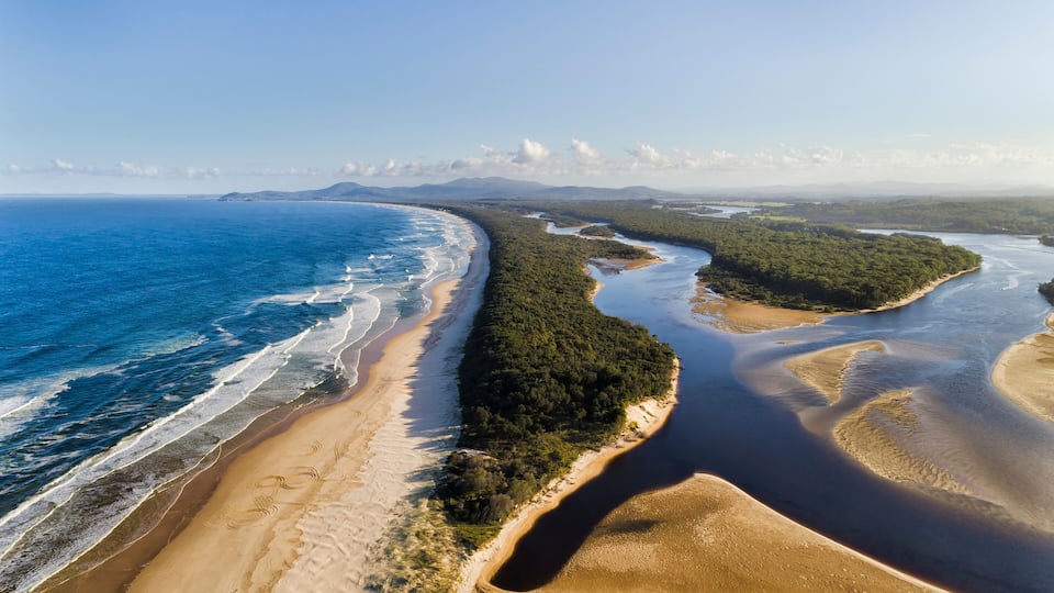 A coastal landscape with a sandy beach, a river, and a forested area.