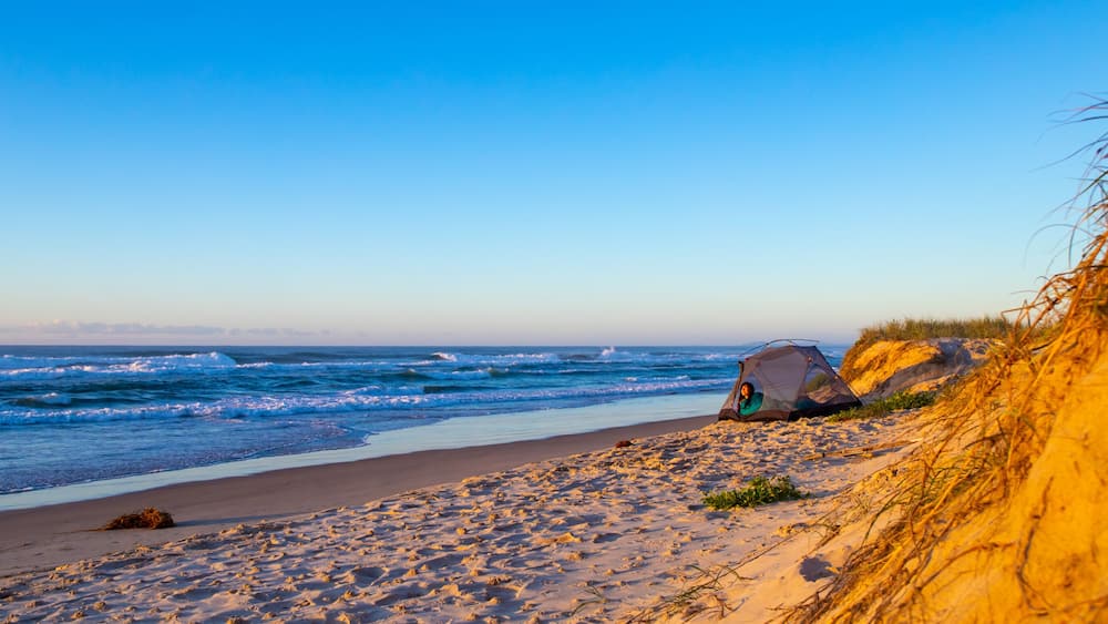 A beach with sand dunes, a tent, and the ocean.