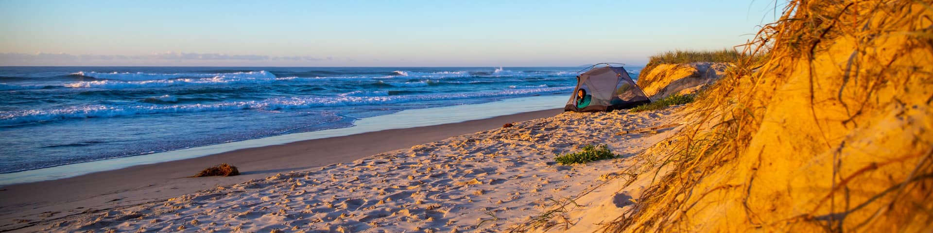 A beautiful girl admires a wonderful sunrise on the beach from her tent. Camping on the beach in Australia, Hat Head National Park, NSW