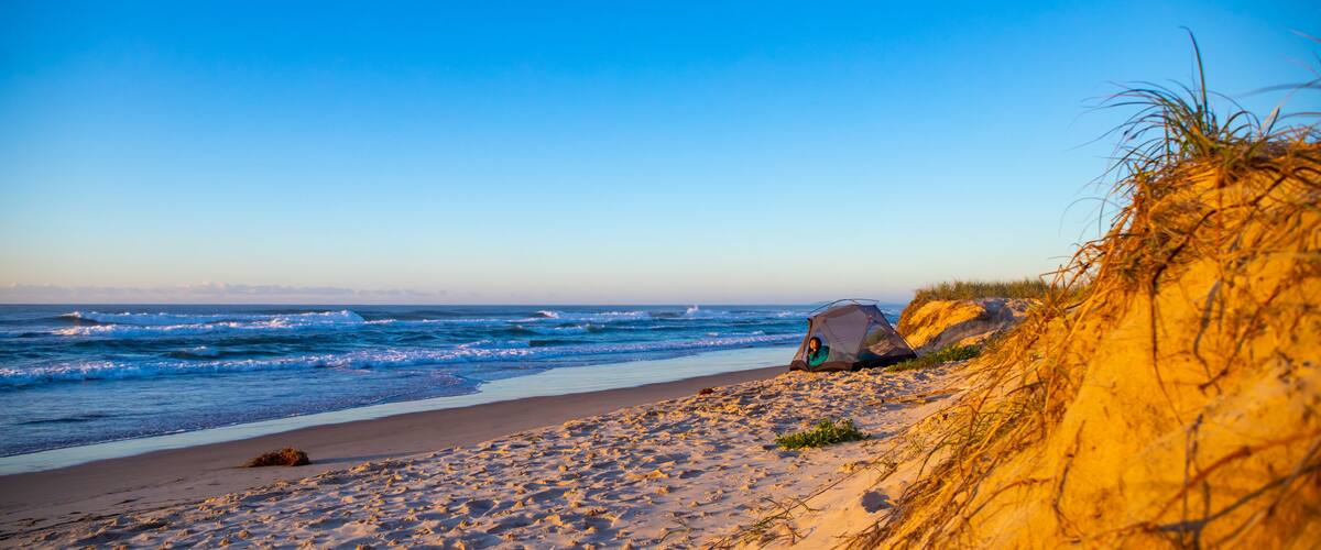 A beach with sand dunes, a tent, and the ocean.