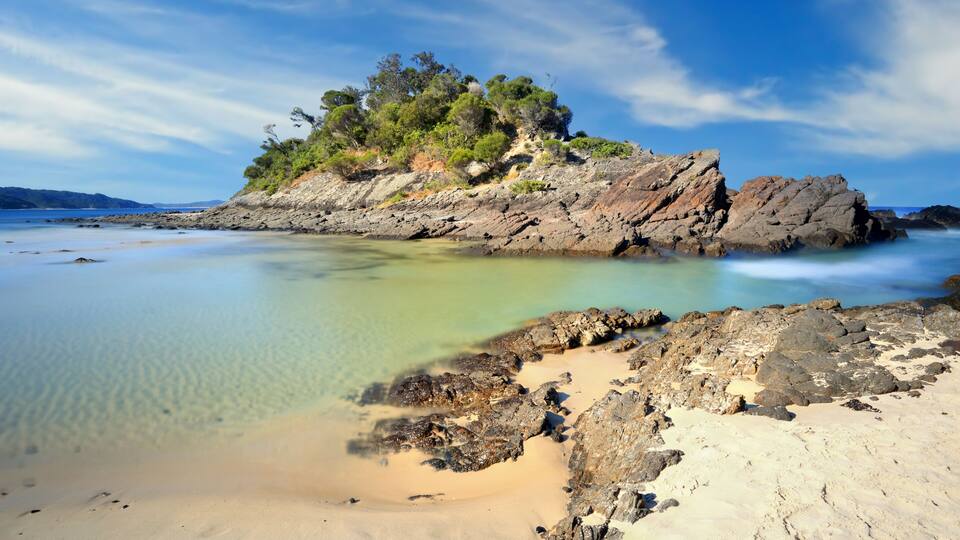 A rocky island with clear turquoise water and sandy beach.