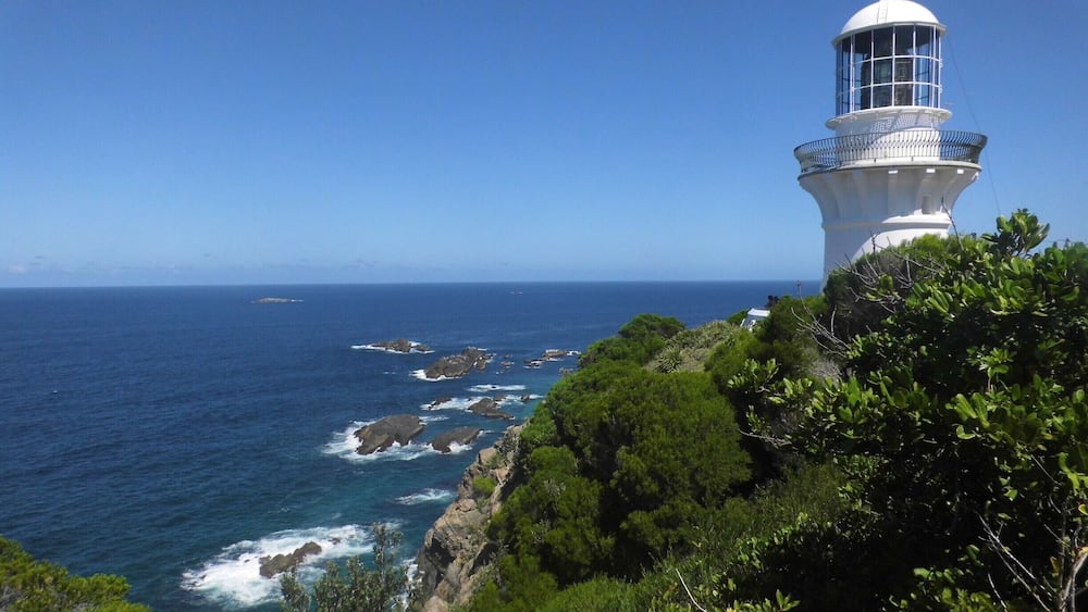 A white lighthouse on a cliff overlooking the ocean.