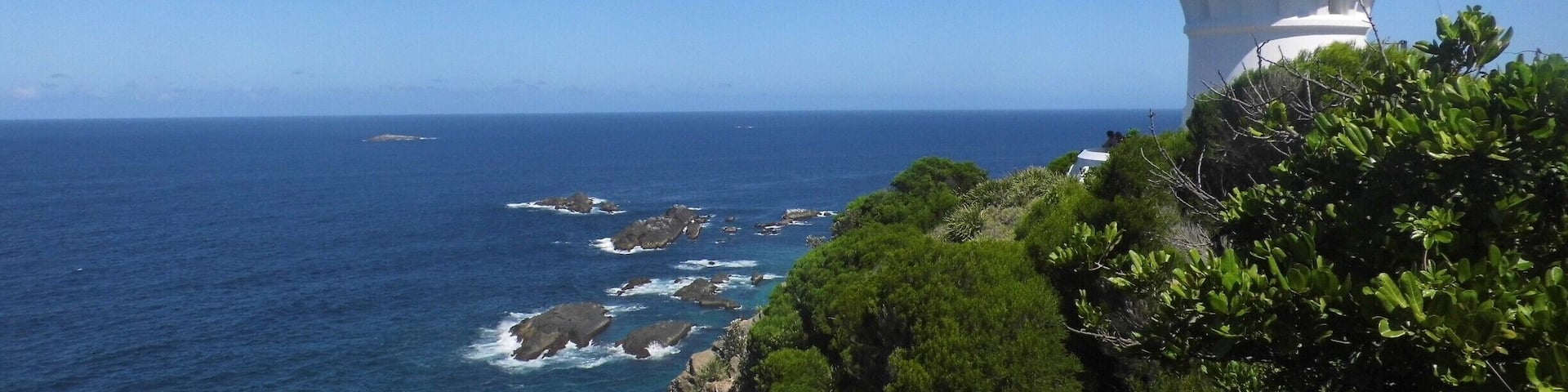 A white lighthouse on a cliff overlooking the ocean.