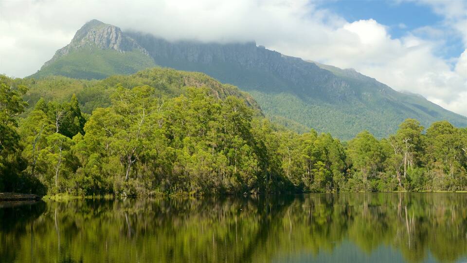 A mountain range with dense green forests and a calm lake reflecting the scenery.