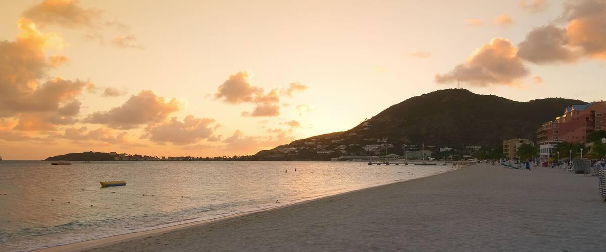 A beach with a boat, a mountain, and buildings in the background.