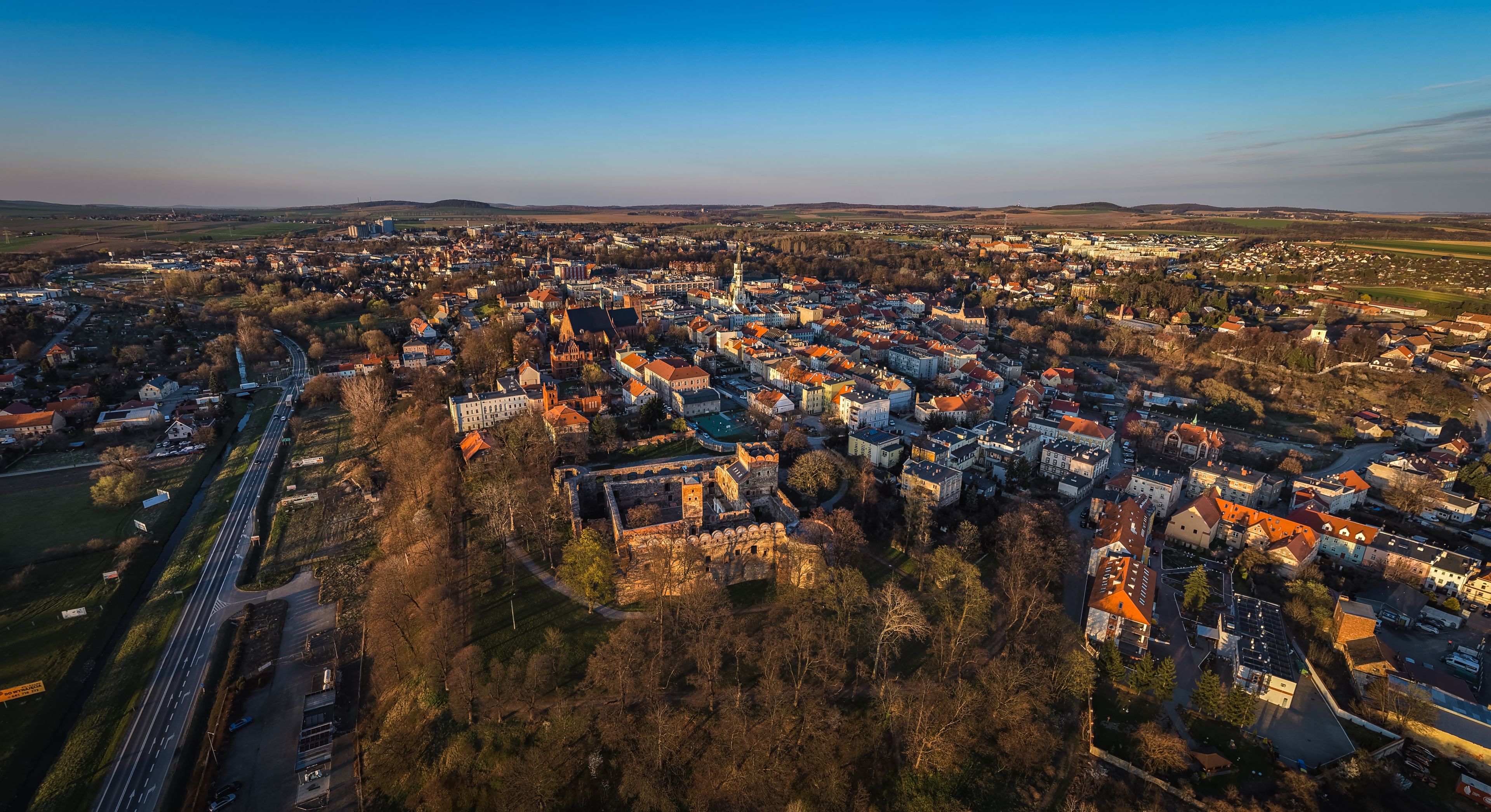 An aerial view of a town with a prominent castle, a main road, and surrounding fields.