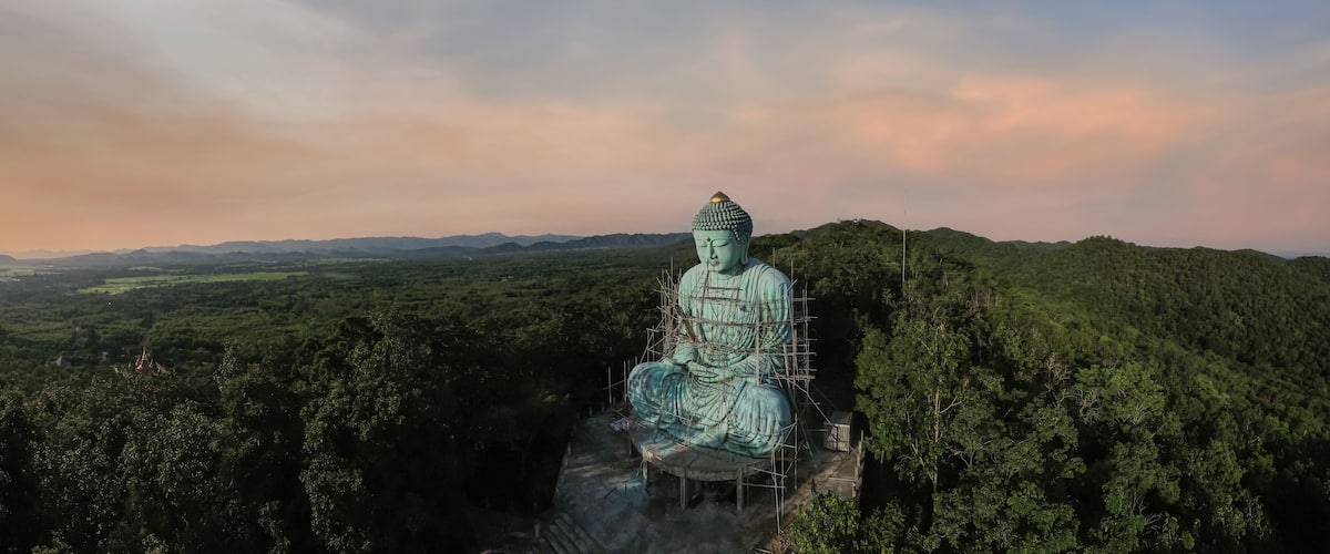 A large Buddha statue surrounded by lush greenery and mountains in the background.
