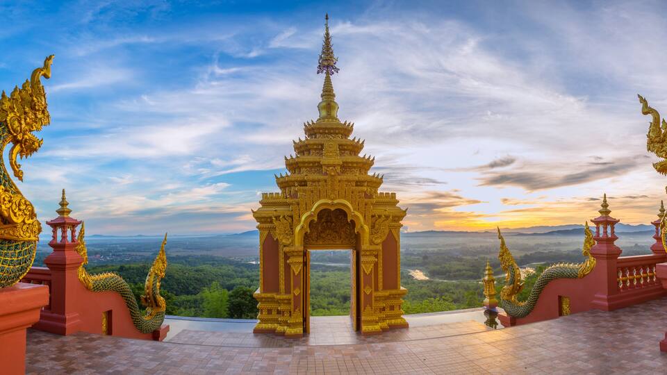 A golden temple with a dragon statue at the entrance, surrounded by lush greenery and a scenic view of the landscape.