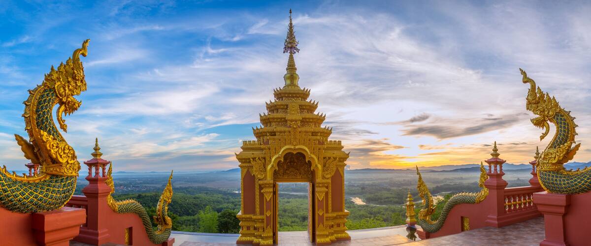 A golden temple with a dragon statue at the entrance, surrounded by lush greenery and a scenic view of the landscape.