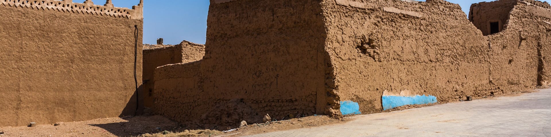 A desert landscape with ancient mud-brick structures and a paved pathway.