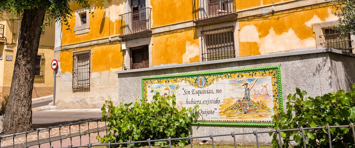 A yellow building with a mural, a tree, and a metal fence.