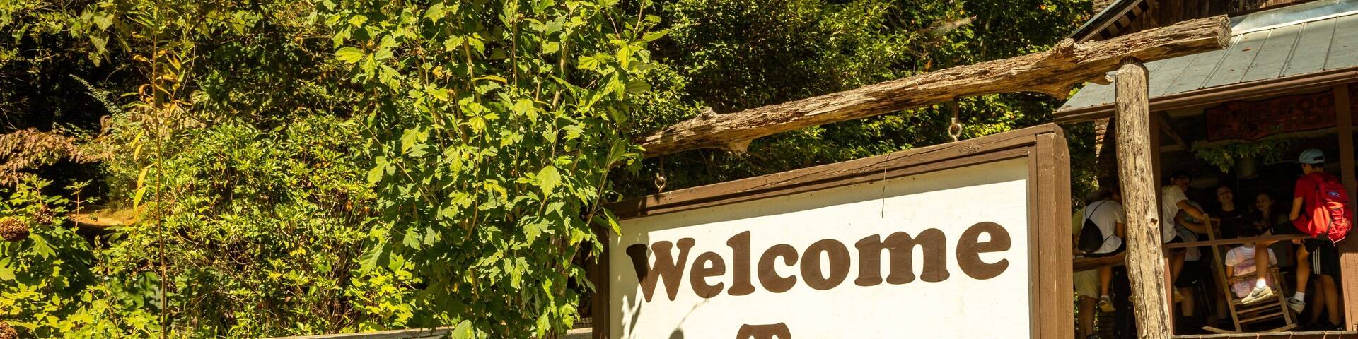 A wooden sign with the text "Welcome To Foxfire" surrounded by greenery.