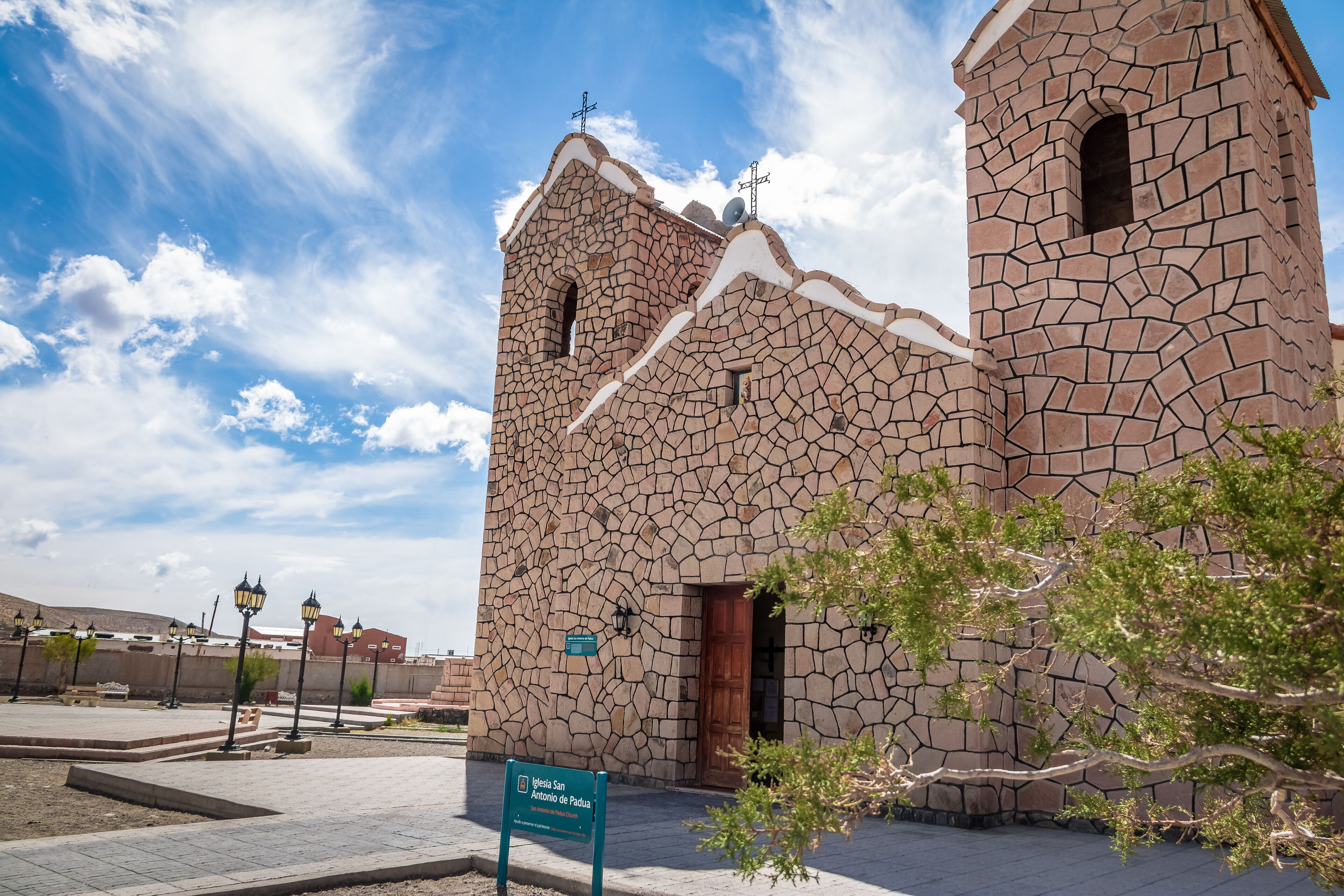 A stone church with a cross on top, a sign in front, and a clear sky.