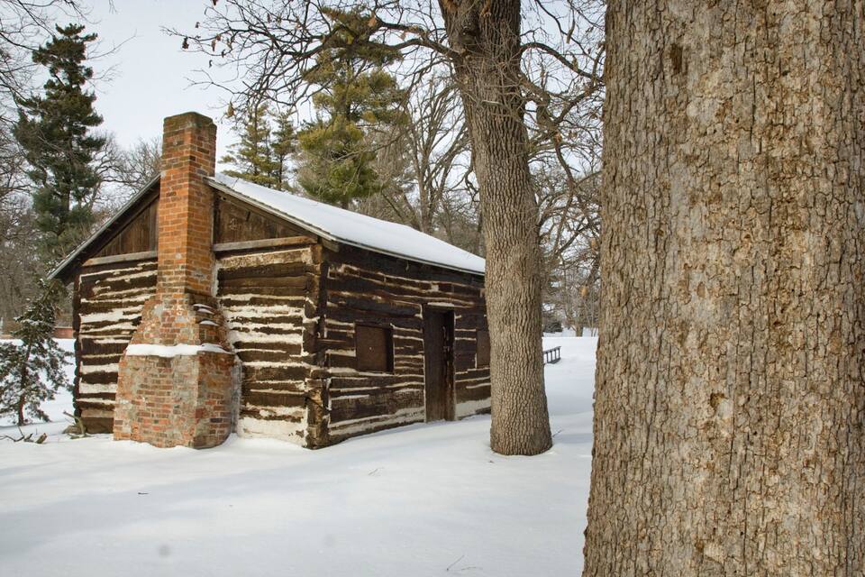 Uma cabana de toras com chaminé de tijolos em uma paisagem nevada.