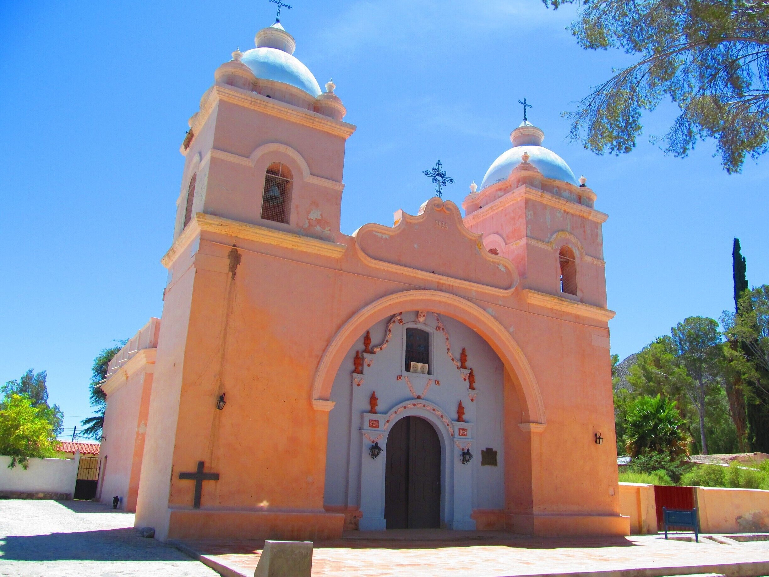 A pink church with two domes and a cross on top.