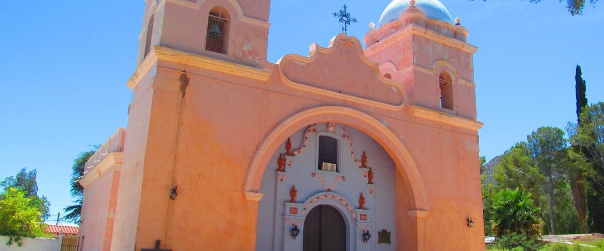 A pink church with two domes and a cross on top.