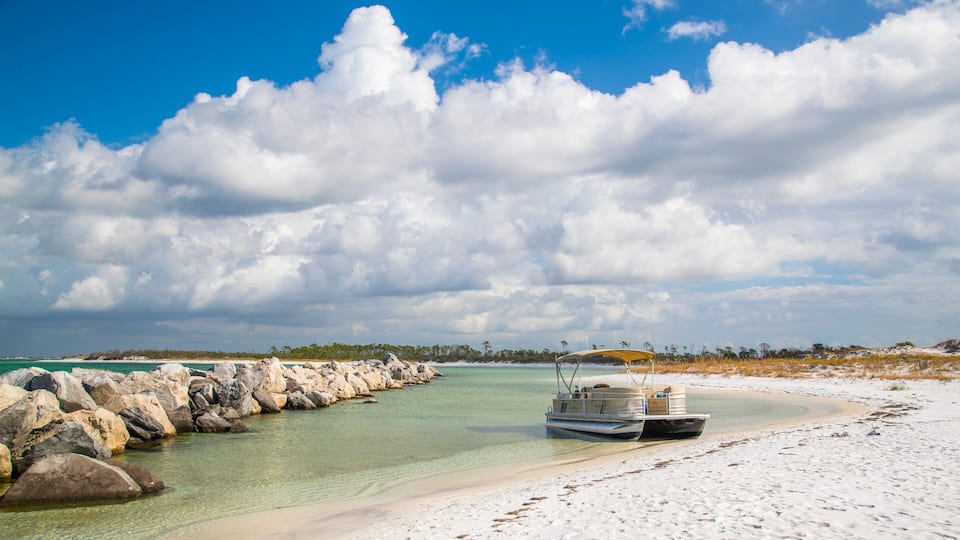 A beach with clear turquoise water, white sand, and a rocky breakwater.