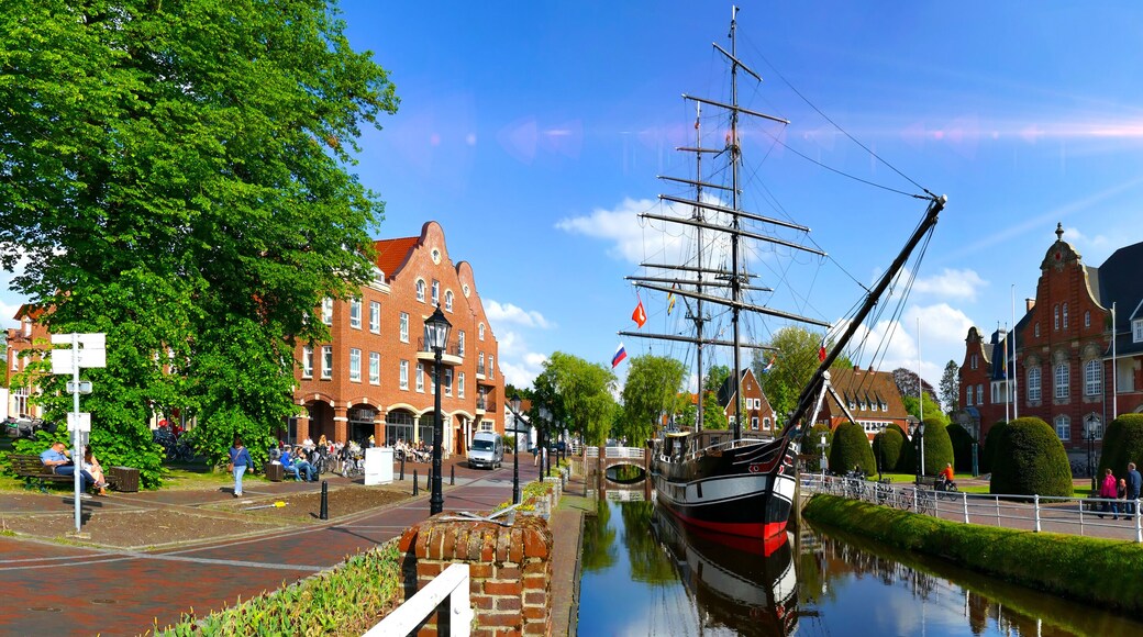 A canal with a tall ship, red brick buildings, and a clear blue sky.