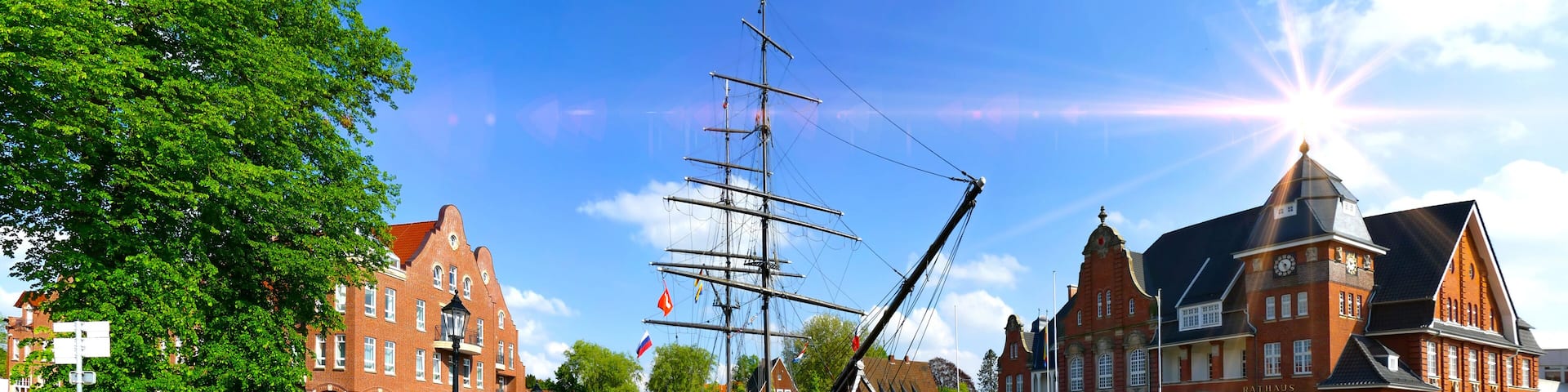 A canal with a tall ship, red brick buildings, and a clear blue sky.