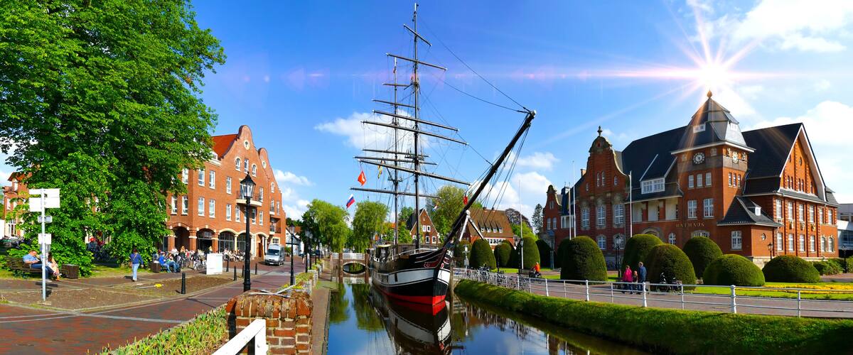 A canal with a tall ship, red brick buildings, and a clear blue sky.