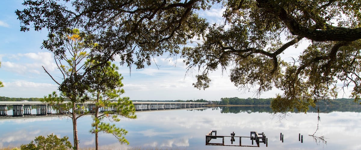 A calm lake with a pier extending into the water, surrounded by trees and grassy areas.