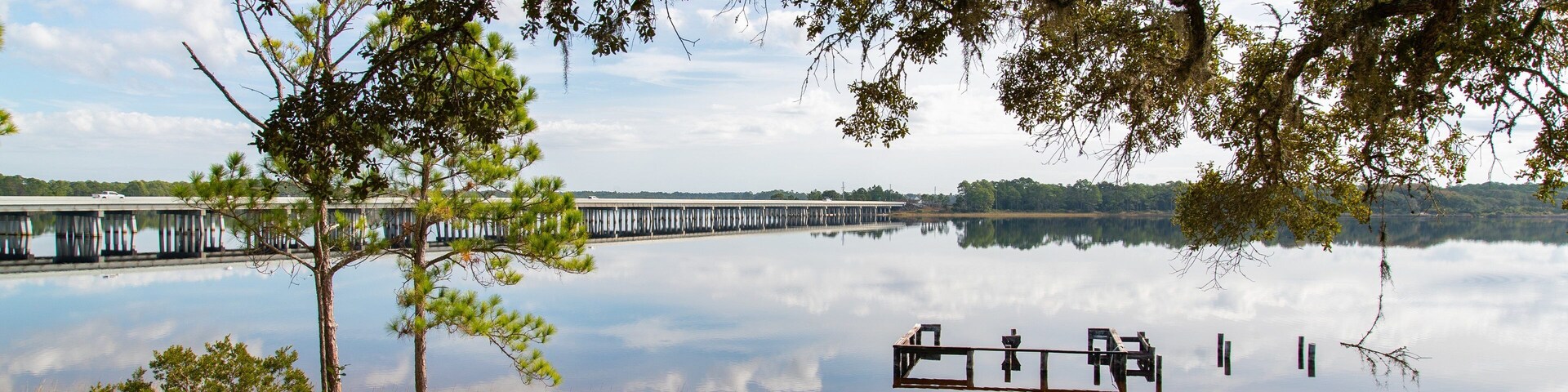 A calm lake with a pier extending into the water, surrounded by trees and grassy areas.