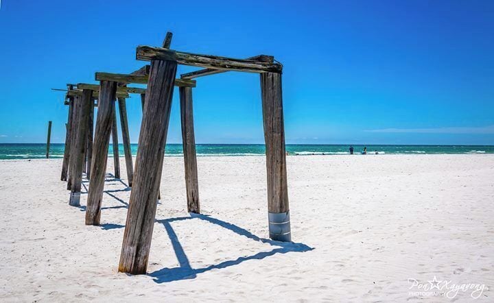 Ein Sandstrand mit Holzgebäuden und dem Meer im Hintergrund.