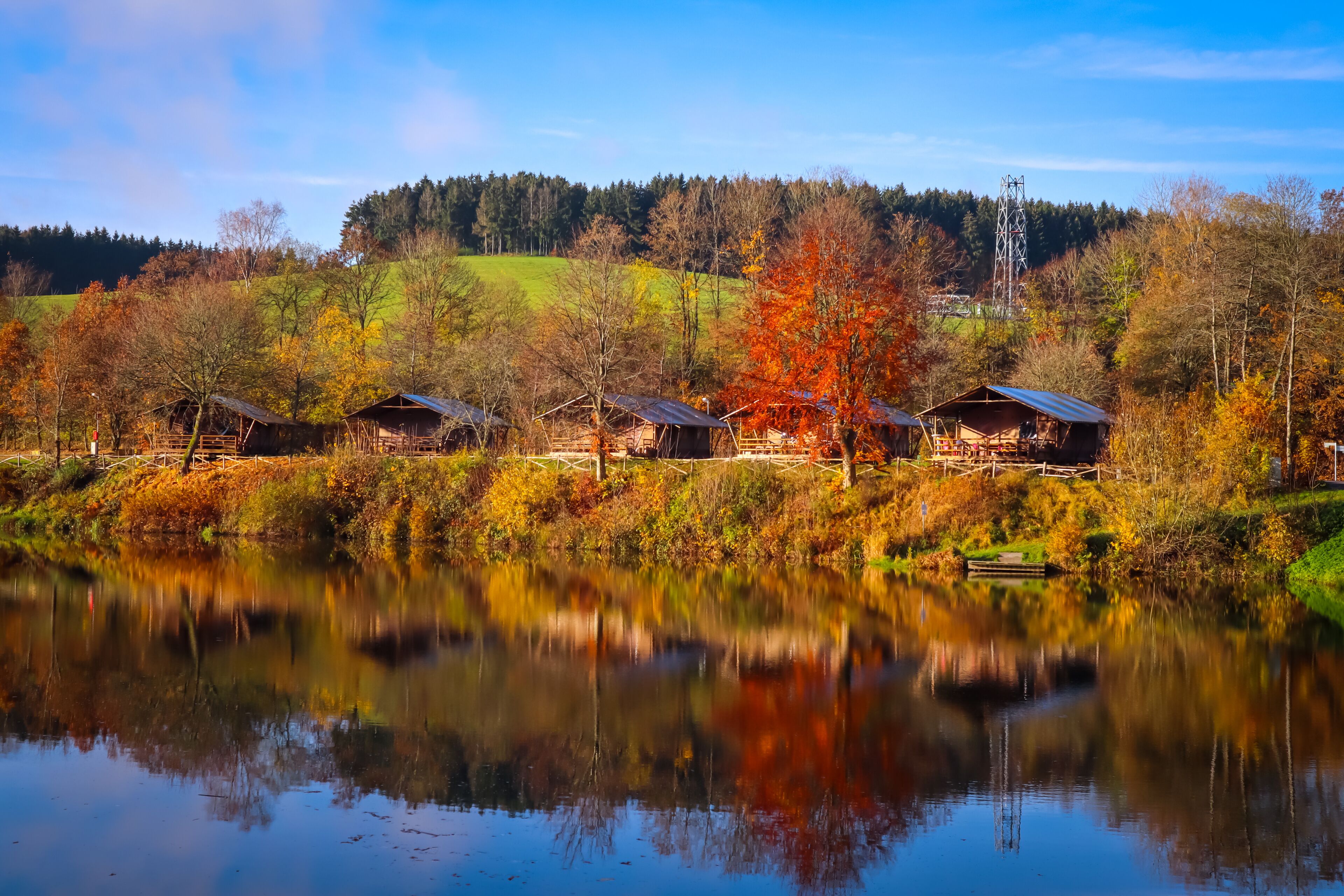 A serene lakeside with wooden cabins and autumn foliage.