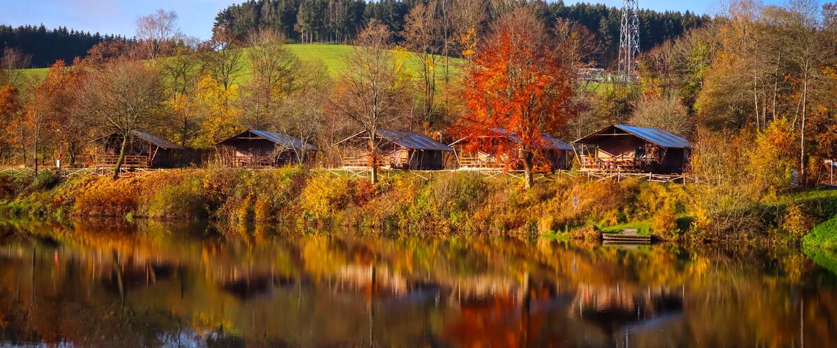 A serene lakeside with wooden cabins and autumn foliage.