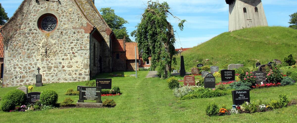 A church with a stone facade and a tower, surrounded by a cemetery with headstones and flowers.