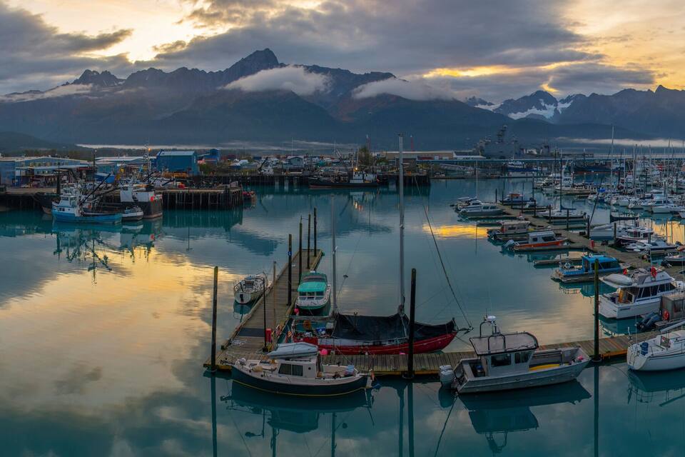 A marina with boats docked, a pier, and mountains in the background.