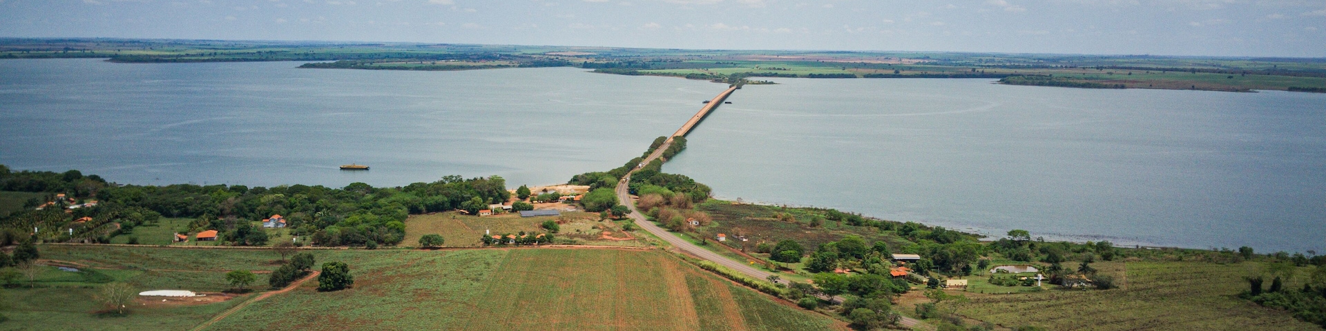 Paisagem costeira com uma longa ponte ligando duas extensões de terra sobre uma vasta área de água.