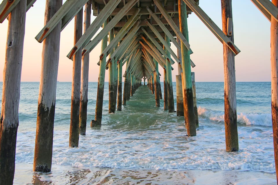 A wooden pier extending into the ocean with waves lapping at its base.