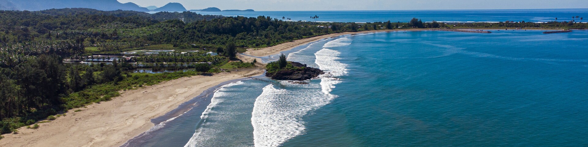 A coastal landscape with a sandy beach, a rocky outcrop, and a clear view of the ocean.