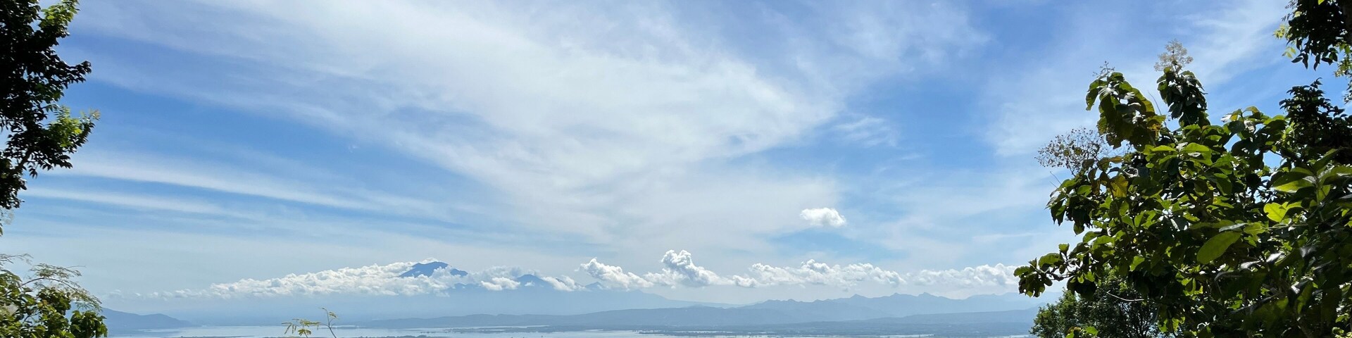 Stunning aerial view of a lush tropical valley in southern Wonogiri, Indonesia, with green fields, lakes, rural villages, and distant mountains under a bright blue sky. footage taken from Pokoh Hill.