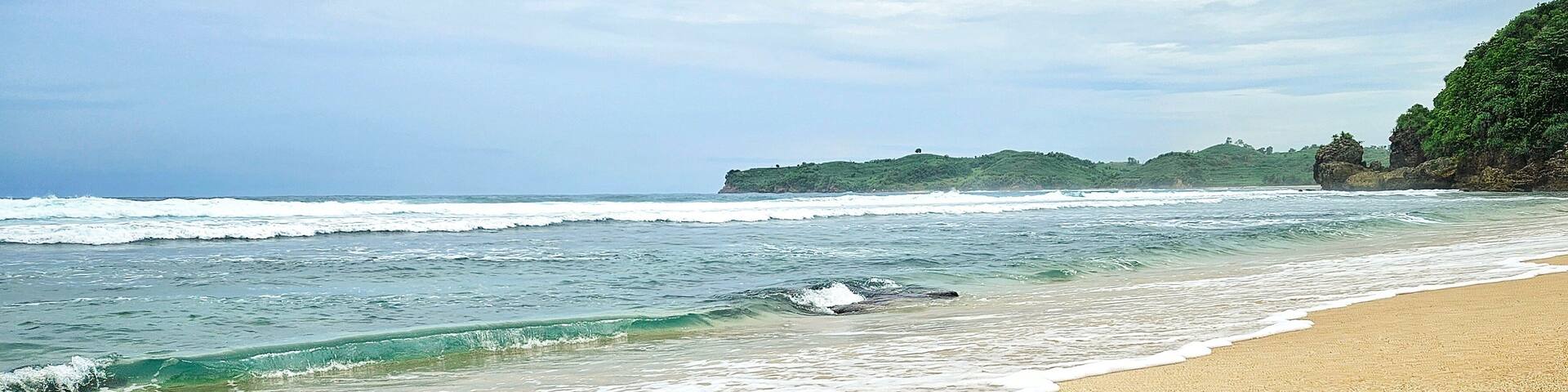 A sandy beach with gentle waves and a rocky outcrop in the distance.