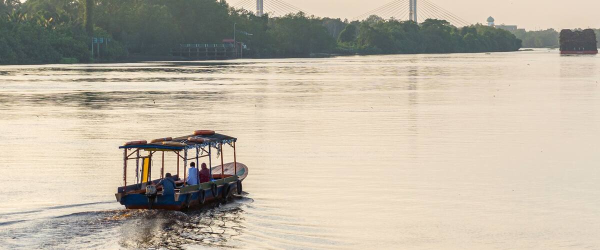 Romantic couple riding a boat down the river at sunset. Couple in traditional boat on Siak river, Riau - Indonesia