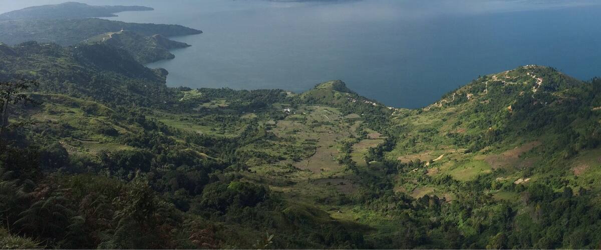 A coastal landscape with rolling hills, a winding road, and a large body of water.