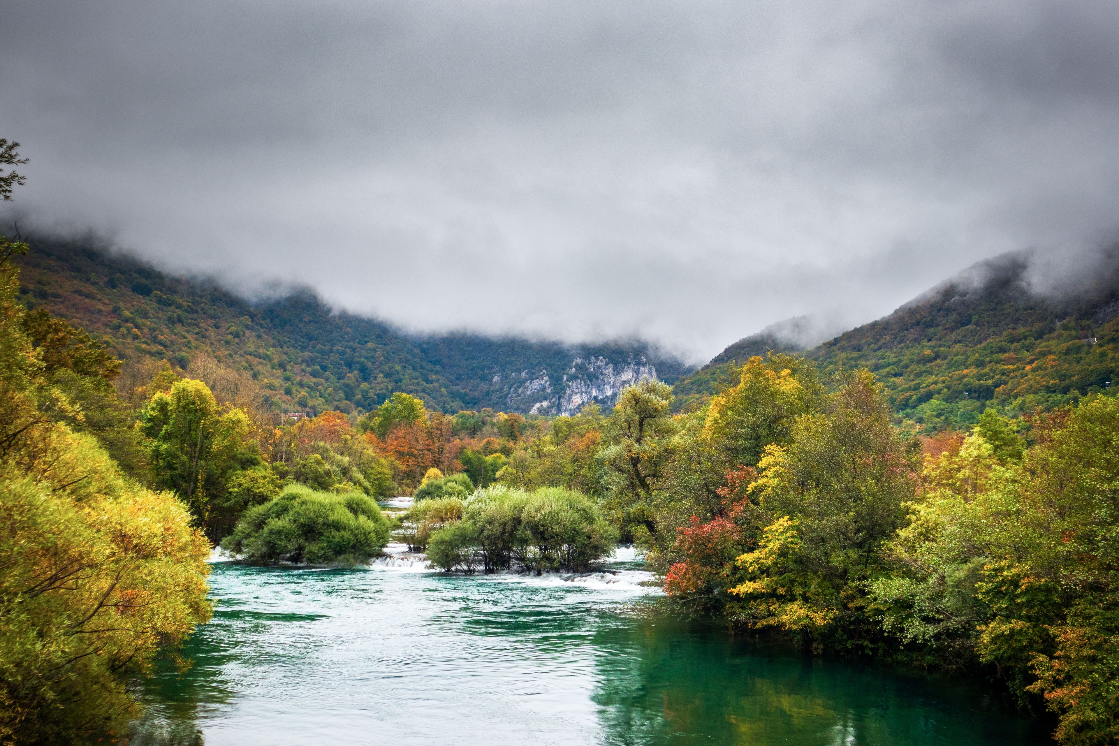 A river flowing through a valley with autumn-colored trees and mountains in the background.