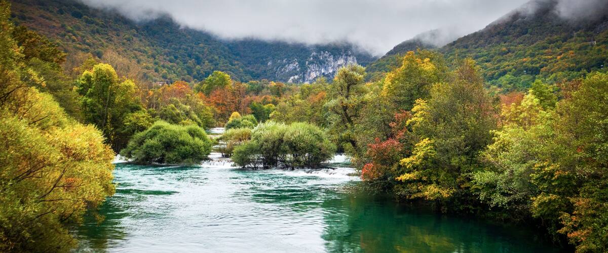 A river flowing through a valley with autumn-colored trees and mountains in the background.