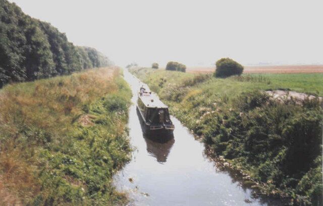 A narrow waterway with a boat in the center, surrounded by lush greenery and a distant horizon.