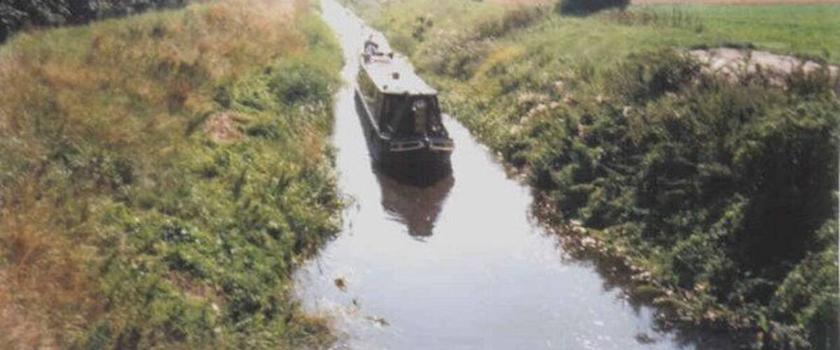 A narrow waterway with a boat in the center, surrounded by lush greenery and a distant horizon.